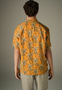 Kurze Ärmel Bluse aus orangefarbenem Stoff mit einem schwarzen Palmenmuster, Knopfleiste am Kragen und einer lässigen Passform. Die strukturierte Oberfläche verleiht Tiefe.