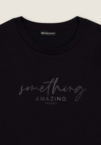 Camiseta negra con cuello redondo y un gráfico metálico plateado que dice "algo ASOMBROSO" en una tipografía estilizada.