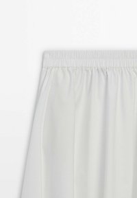 Gonna bianca plissettata con vita elastica, caratterizzata da una texture liscia e priva di motivi o dettagli in metallo visibili.
