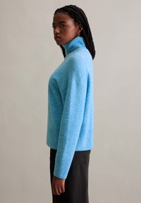 Helles blaues Rollkragensweatshirt aus weichem, strukturiertem Strick; hat eine lockere Passform und gerippte Bündchen; kombiniert mit dunklen Hosen.