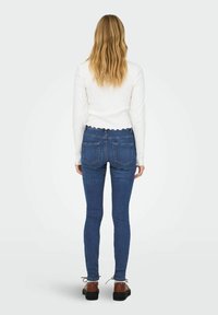 Sinised kitsad teksad, millel on sile denimistruktuur ja kaks tagakotti, koos valge pika varrukaga särgi kanssa, millel on laineline äär.