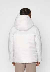 Weißer isolierter Mantel mit großer Kapuze, der eine glatte Textur, elastische Bündchen und einen leichten Glanz aufweist. Einfaches, minimalistisches Design.