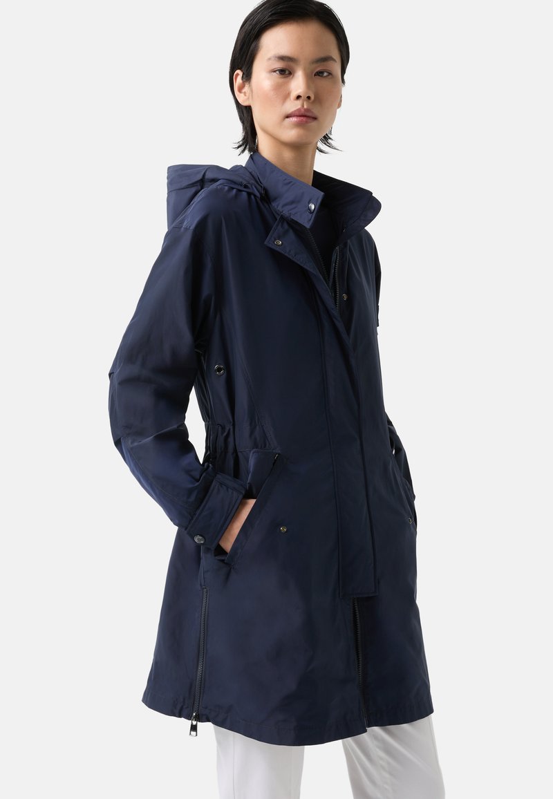 Nepromokavá parka navy modré barvy s kapsami na zip, nastavitelnou kapucí a stahovacími šňůrkami v pase. Vyznačuje se hladkým povrchem a minimalistickým designem.