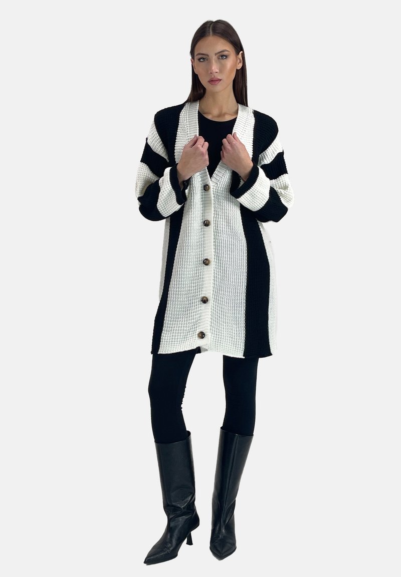 Sort og hvid strikket cardigan med en løs pasform, der har horisontale striber, en knaplukning foran og brede ærmer. Sorte knæhøje støvler.