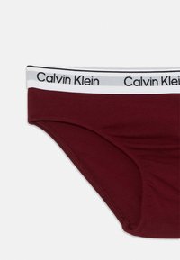 Bordové bavlnené nohavičky s bielym elastickým pásom, na ktorom je čierny nápis "Calvin Klein". Hladký povrch, klasický dizajn spodnej bielizne.