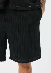 Pantalones cortos negros de textura con canalé vertical, costuras blancas en contraste, bolsillos laterales y un corte relajado.