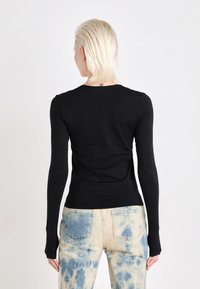 Svart langermet tettsittende topp i en glatt stoff, med rund hals og kroppsformet design, kombinert med mønstrede lyseblå jeans.