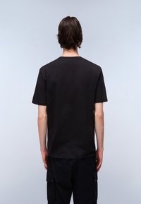 Zwarte katoenen t-shirt met een ronde hals, korte mouwen en een rechte snit, weergegeven van de achterkant tegen een lichte achtergrond.