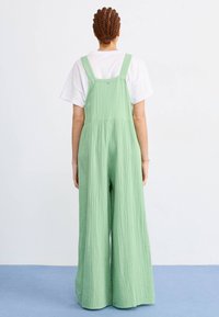 Groene, lichtgewicht, gekreukelde stof salopette met wijde benen, verstelbare bandjes en een ontspannen pasvorm, gecombineerd met een wit T-shirt eronder.