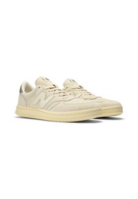 Pair of beige suede New Balance sneakers with laces, perforated toe box, and rubber soles, shown at a slight angle on white background.