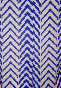 Tkanina z niebieskim wzorem w zygzaki na jasnym tle, prezentująca wyraźne kształty chevron o miękkiej fakturze i wyraźnych liniach.