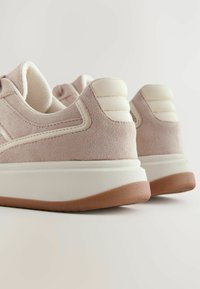 Baskets en suede rose clair avec un accent en cuir couleur crème, semelle en caoutchouc texturé et détails de talon surélevés. Design arrondi avec rembourrage.