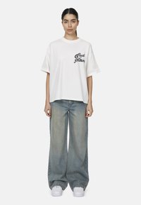 T-shirt in cotone bianco con la scritta "Good for Nothing" stampata in nero, abbinata a jeans in denim azzurro a gamba larga e sneakers bianche.