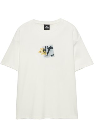 Bijela kratki rukav T-shirt s malim grafičkim prikazom nečijih nogu koje hodaju i žutim cvjetovima na lijevoj strani prsnog dijela.