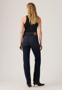 Σκούρο μπλε τζιν παντελόνι με ευθεία γραμμή στα πόδια, διαθέτοντας πίσω τσέπες με χαρακτηριστική ραφή και καφέ δερμάτινη ετικέτα στη μέση.