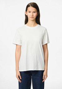 Valkoinen puuvillapaita, jossa on lyhyet hihat, pyöreä kaula-aukko ja rento istuvuus, yhdistetty tummansinihin farkkuihin. Sileä pinta ilman näkyviä kuvioita.