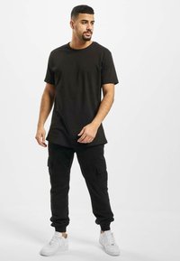 Zwarte T-shirt met korte mouwen, gecombineerd met zwarte cargobroek. De outfit wordt vervolledigd met witte sneakers, die een eenvoudig, casual ontwerp hebben.
