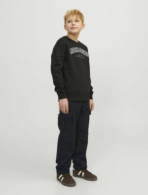 Svart sweatshirt med vit text, mörka cargobyxor och bruna sneakers med vita ränder. Rakt snitt, enkel design och bomullstextur.