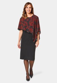 Zwarte jurk met een knielange silhoette, gecombineerd met een doorschijnende, bloemenpatronen cape in rood en zwart. Voorzien van zwarte hoge hakken.