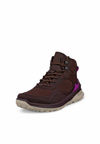 Scarpa alta marrone con tomaia in tessuto testurizzato, lacci elastici, dettagli viola e suola beige chiaro. Presenta sovrapposizioni con motivo.
