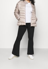 Beige puffjacka med glänsande yta, med horisontellt kviltad design, dragkedjestängning och tryckknappskrage, matchad med svarta utsvängda byxor och vita sneakers.