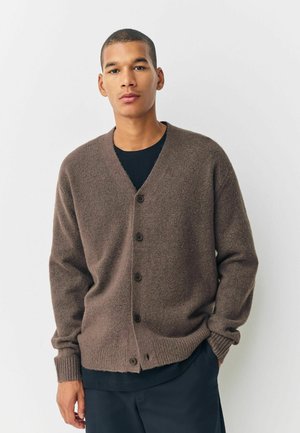 Brown wool cardigan with a V-neck, long sleeves, and five-button front closure. Ribbed cuff and hem detailing. Worn over a black shirt.