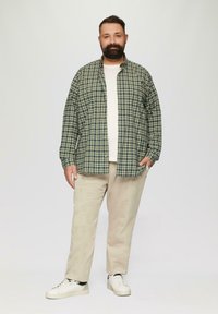 Groen en marineblauw geblokt overhemd over een wit T-shirt, gecombineerd met beige corduroy broek en witte sneakers.