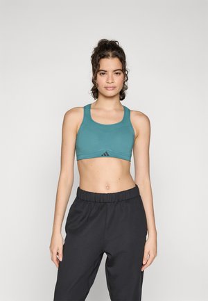 Teal sports bra with thick straps, a scoop neckline, and a logo detailing. Paired with black, elastic waist workout pants.