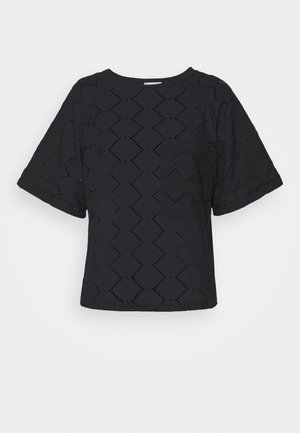 Zwarte blouse met korte mouwen, zigzag uitsnijdingen en een ronde halslijn, afgebeeld tegen een eenvoudige lichte achtergrond.