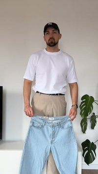 Lyseblå denimjeans med frontlommer og knappelukking. Modellen har på seg en hvit skjorte og beige bukser, med et svart belte.