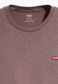 Mauve crew-neck t-shirt från Levi's med röd Levi's-logotyp på framsidan samt tryckta storleks- och tillverkningsdetaljer inuti kragen.