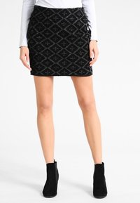 Svart, texturerad kjol med diamantmönster, figursydd design, knälång, tillsammans med svarta ankellångstövlar. Långärmad topp i ljus färg.