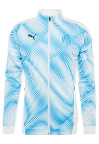 Světle modrá sportovní bunda s vlnitým vzorem, bílými akcenty, zipem a logem Puma na hrudi. Vyrobena z hladkého, sportovního materiálu.