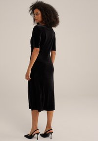 Black velvet midi dress with short sleeves, a fitted waist, and a soft, smooth texture. Paired with sleek black slingback heels.
