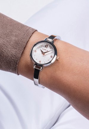 Montre Furla avec un boîtier rond en acier inoxydable argenté, un cadran texturé blanc, des accents en or rose et un bracelet en cuir noir poli.