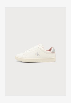 Baskets basses blanches avec doublure intérieure rose, lacets à l'avant et logo Calvin Klein sur le côté sur fond gris clair.