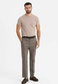 Béžové přiléhavé tričko doplněné šedými kalhotami na míru se plochým předním dílem, bočními kapsami a černým opaskem. Hnědé boty dokončují vzhled.