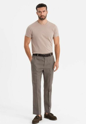 Beiger, taillierter T-Shirt kombiniert mit grauen, maßgeschneiderten Hosen, die eine flache Vorderseite, seitliche Taschen und einen schwarzen Gürtel aufweisen. Braune Schuhe runden den Look ab.