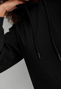 Sudadera negra hecha de una tela suave, con un bolsillo tipo canguro, cordones ajustables y un diseño de ajuste relajado.