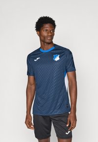 Maglia sportiva blu navy con motivo a righe orizzontali, maniche corte e accentuazioni blu a contrasto. Include un logo sul petto.