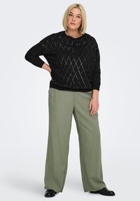 Black diamond-patterned knitted sweater, oversized fit, paired with sage green wide-legged trousers. Model wears black shoes.
