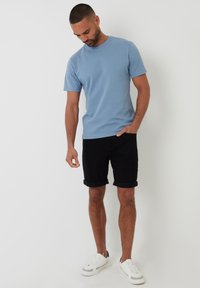 Světle modré tričko s krátkým rukávem a kulatým výstřihem, doplněné černými šortkami s ohrnutými nohavicemi a bílými teniskami. Hladký textilní povrch.