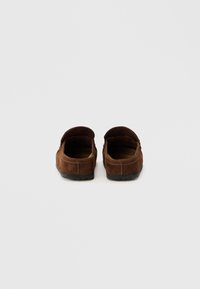 Καφέ δερμάτινα μοκασίνια από σουέντ με στρογγυλερή μύτη, απαλή υφή και χαμηλή λαστιχένια σόλα. Σχεδιασμός ανοιχτής πλάτης με ραφές κατά μήκος της άκρης.