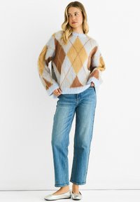 Light blue knitted sweater with a diamond pattern in brown and cream. Paired with mid-blue straight-leg jeans and silver flats.