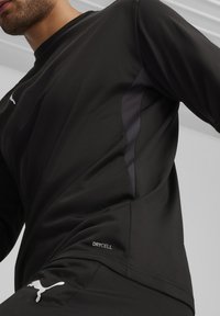 Zwart sportshirt met lange mouwen, gemaakt van vochtregulerende stof met een gestructureerd zijpaneel. Het shirt heeft een subtiele logo en "DRYCELL" detail.