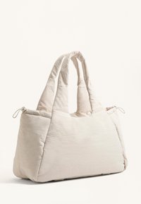 Beige, quiltet tote taske med to forlængede håndtag, indsnørede kanter og blød tekstur. Har en afslappet form og minimalistisk design.