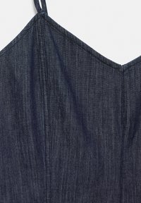 Tissu en denim bleu foncé avec des coutures verticales visibles et une fine bretelle sur un vêtement sans manches.
