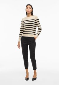 Beige sweater with black horizontal stripes, round neckline, and long sleeves. Paired with black fitted trousers and black pointed heels.