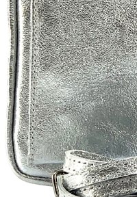 Sac en cuir argenté à porter en bandoulière avec une surface texturée, doté d'une fine sangle réglable et de bords cousus propres.