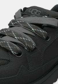 Black sneaker with textured surface and gray accent details. Features dark gray laces with a checkered pattern and rubber sole.